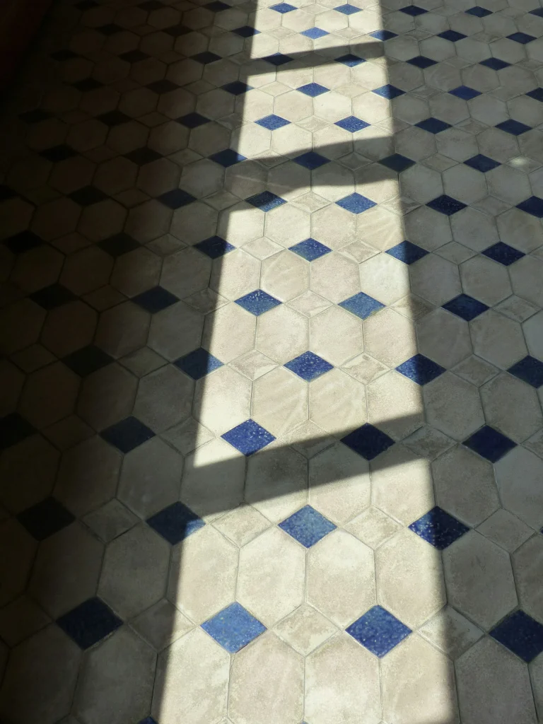 Vecchio pavimento piastrellato a esagoni con fughe scurite, illuminato da luce radente
